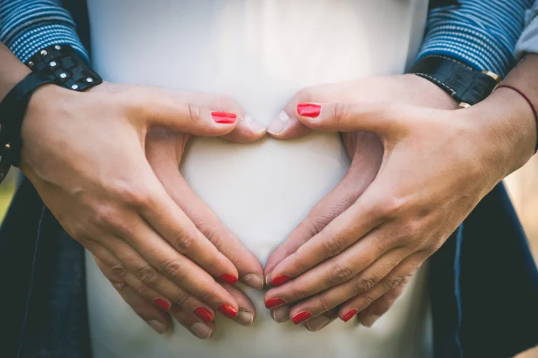 Pregnant couple holding belly in heart shape